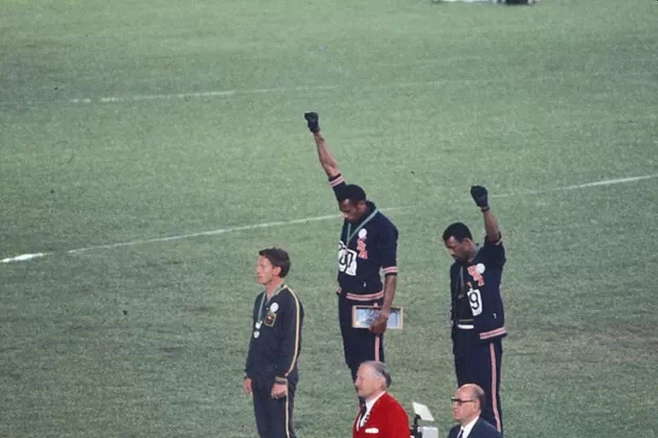 Tommie Smith (no alto do pódio) e John Carlos com os punhos erguidos no pódio dos 200 metros em 1968.