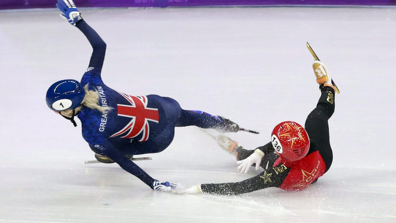 Li Jinyu (CHN, capacete 136) cai no gelo e atinge Elise Christie (GBR, capacete 1) na semifinal dos 1.500 metros em PyeongChang-2018. Foto: How Hwee Young/EFE/EPA