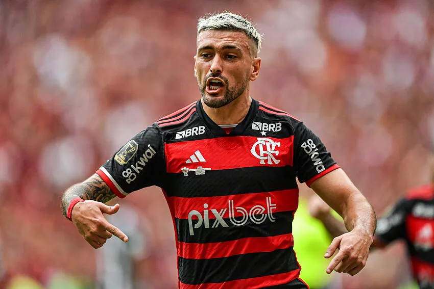 Arrascaeta comemorando um gol pelo Flamengo, com a torcida desfocada ao fundo